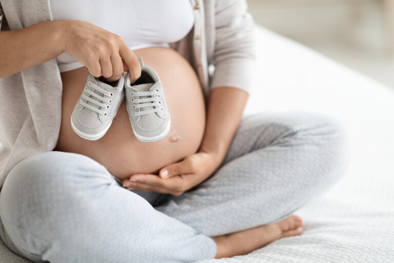 cropped pregnant woman holding baby shoes big tummy