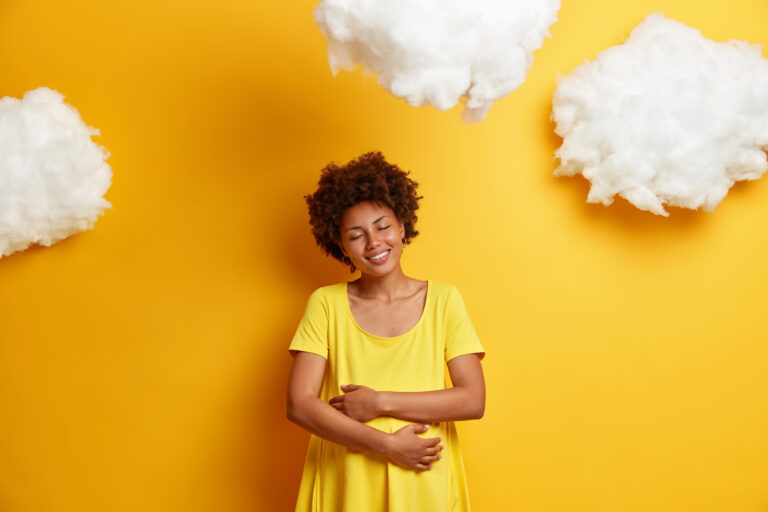 pleased african american woman embraces pregnant belly expresses love unborn child smiles happily enjoys last months pregnancy isolated yellow wall expectant mother hugs tummy